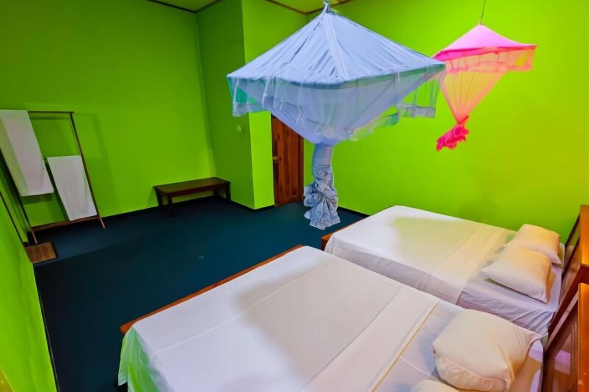 Habitación con dos camas, un banco, una mosquitera y un espejo.
