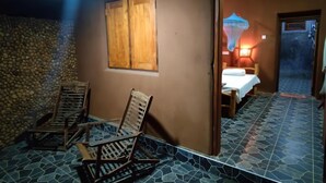 A room with a stone wall, a wooden door, and a bed with a white sheet. - Elephant Paradise Safari Lodge (Udawalawa)