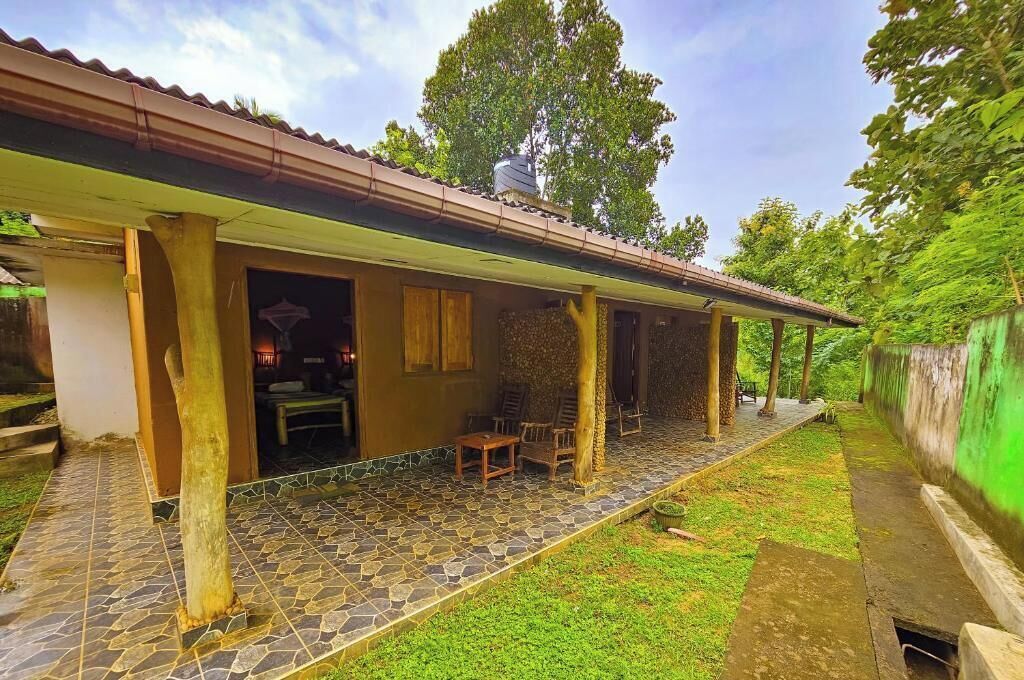 A covered outdoor area with a stone-tiled floor, wooden furniture, and a green wall.