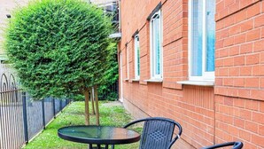 A small outdoor seating area with a round table and two chairs, surrounded by a brick wall and a hedge.
