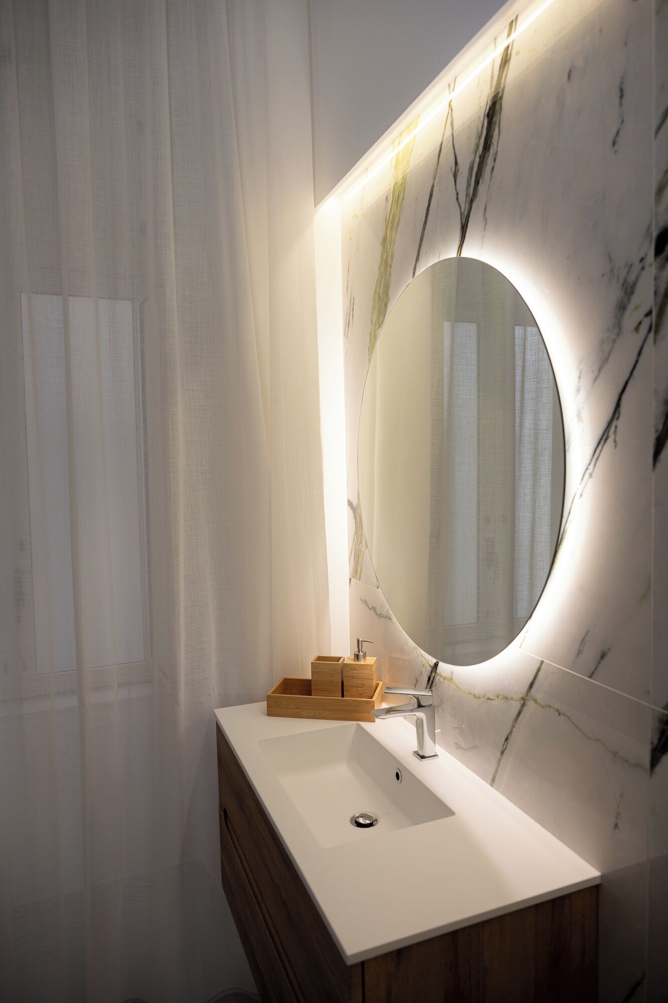 Ein modernes Badezimmer mit Marmor-Waschtisch, einem großen Spiegel und einem Holzkabinett.