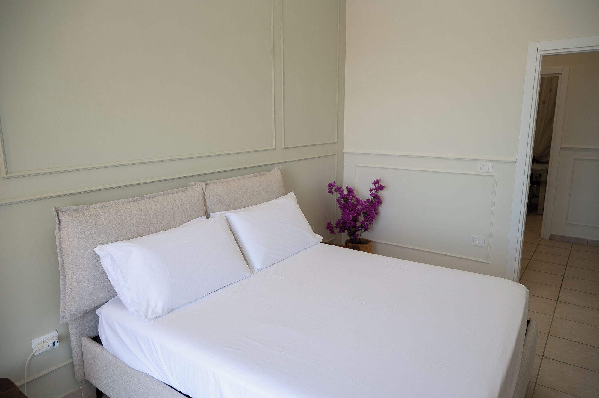 Een net opgemaakt bed met witte lakens in een kamer met lichte muren en een houten vloer.