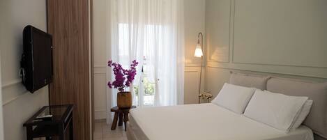 A bedroom with a bed, a TV, a wooden wardrobe, a small table with a vase of flowers, and a bedside lamp.
