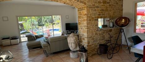 Uma sala de estar ampla com parede de pedra, um sofá, uma TV e um espaço de jantar com mesa e cadeiras.