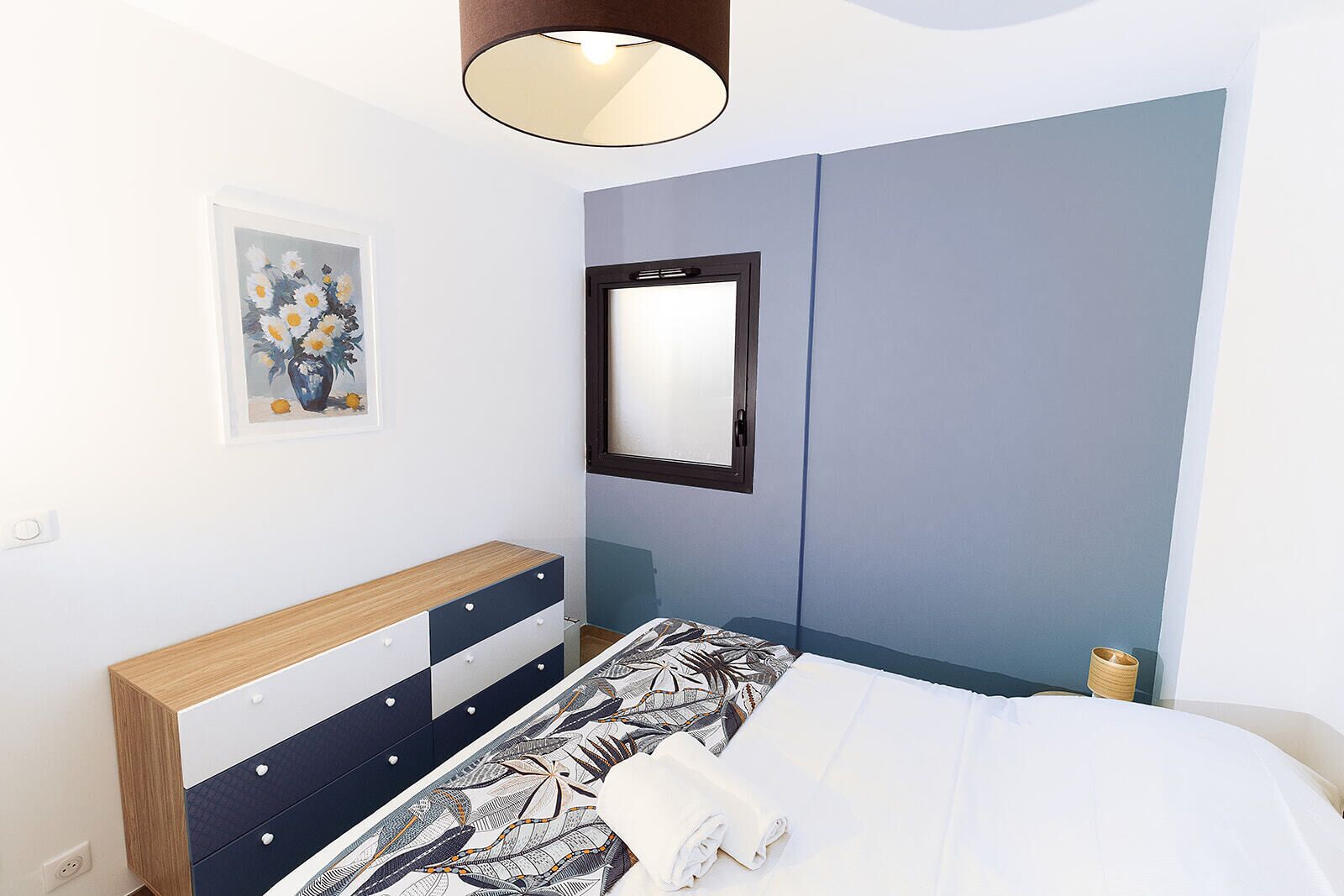 A bedroom with a bed, a bedside table, a dresser, a mirror, and a painting on the wall.