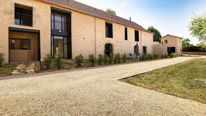 Un bâtiment moderne avec une allée en gravier, un petit jardin et un espace patio doté de meubles pour se détendre en plein air.