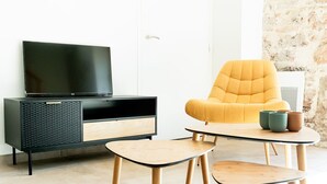 Un salon moderne avec un meuble de rangement noir pour les appareils électroniques, un fauteuil de couleur moutarde et deux petites tables en bois.