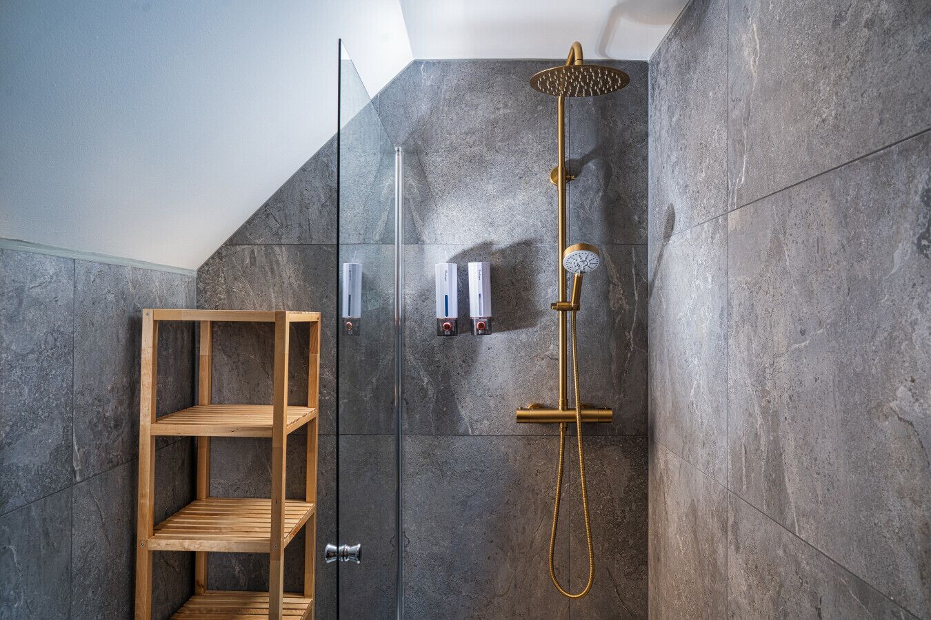 Een moderne douche met een gouden douchekop en een glazen cabine.