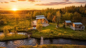 Un ensemble de chalets situés au bord d’un lac, avec une jetée en bois, entourés de forêt et traversés par une rivière.