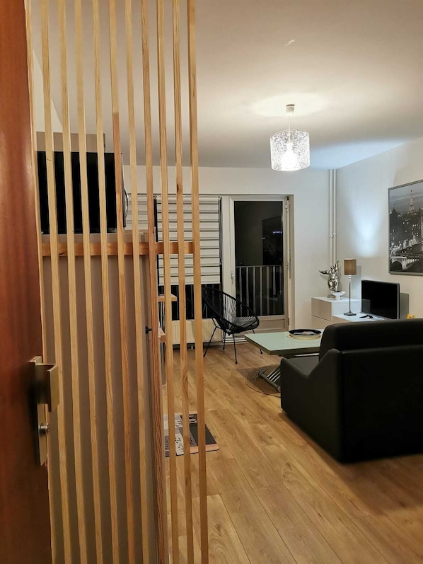 A modern living room with a wooden floor, a black sofa, a dining table, and a black chair. There is a staircase leading to another level, and a large window with a view of the outside. - Center Reims Moderne with balcony and parking (Reims)