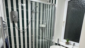 Une salle de bain avec une douche à parois de verre, un lavabo blanc et un meuble-lavabo vert.