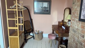 Une pièce comprenant une armoire en bois, une chaise, un petit tabouret, un tableau encadré accroché au mur, ainsi qu’une commode avec un miroir et une lampe.
