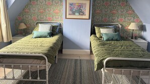 Une chambre avec deux lits simples, un mur décoré d’un motif, un tableau encadré et une lucarne.
