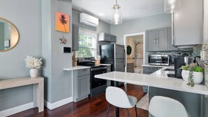 A modern kitchen with grey cabinets, a white countertop, and stainless steel appliances. There is a dining area with two chairs and a small table.