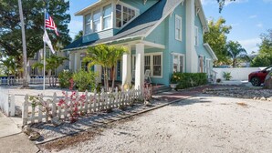 A two-story house with a porch, a flag, and a gravel driveway.