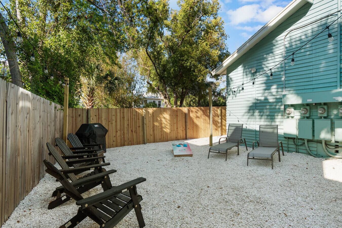 Un patio trasero con cerca de madera, una parrilla y mobiliario exterior con sillas y una mesa.