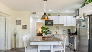 Una cocina moderna con armarios blancos, un refrigerador de acero inoxidable y un comedor con mesa de madera y sillas blancas.
