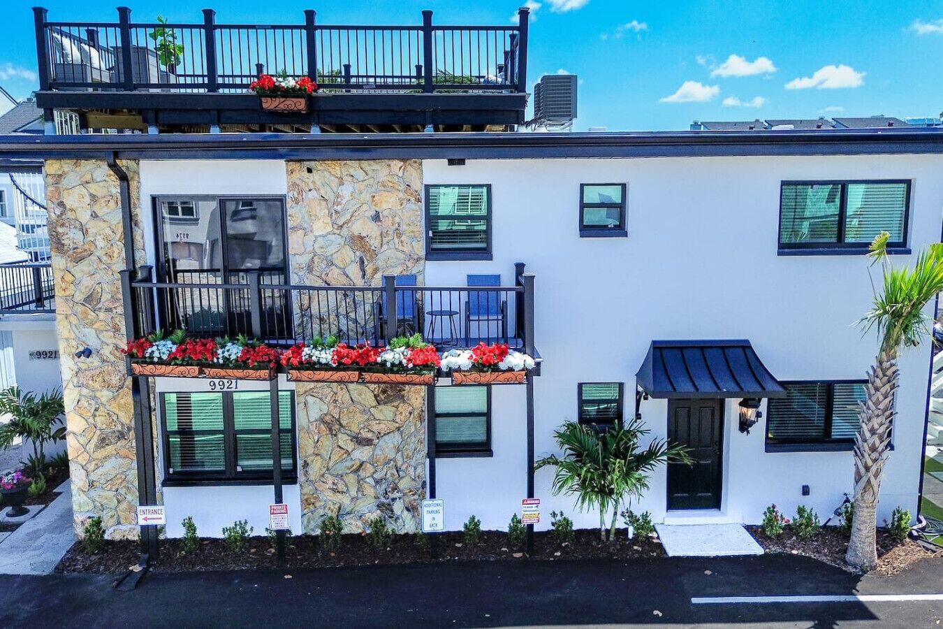 A modern two-story building with a stone facade, balconies with flower boxes, and a small entrance sign.