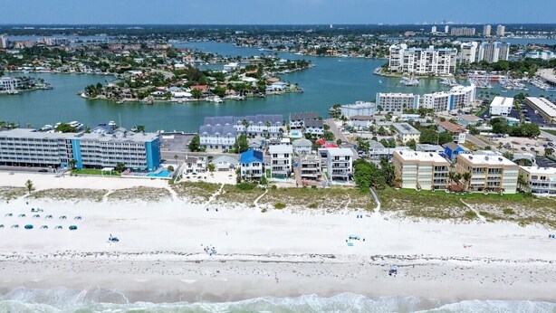 Un paisaje urbano costero con un hotel frente a la playa, un puerto deportivo y edificios residenciales.