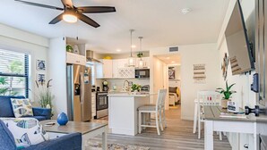 A modern kitchen with white cabinetry, a central island, and a dining area with white chairs.