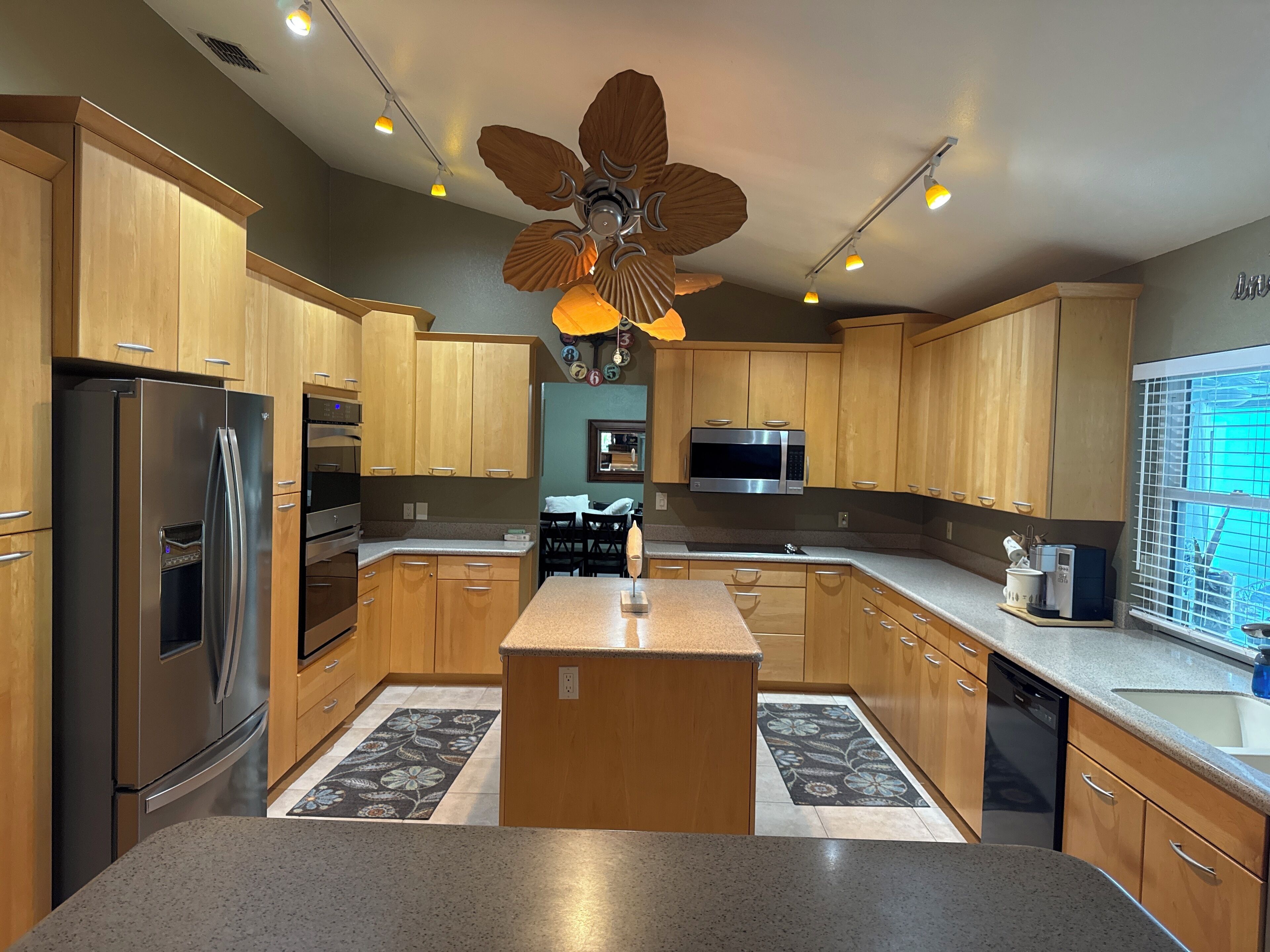 A modern kitchen with wooden cabinets, stainless steel appliances, a central island, and a ceiling fan.