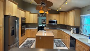Una cocina moderna con gabinetes de madera, electrodomésticos de acero inoxidable, una isla central y un ventilador de techo.