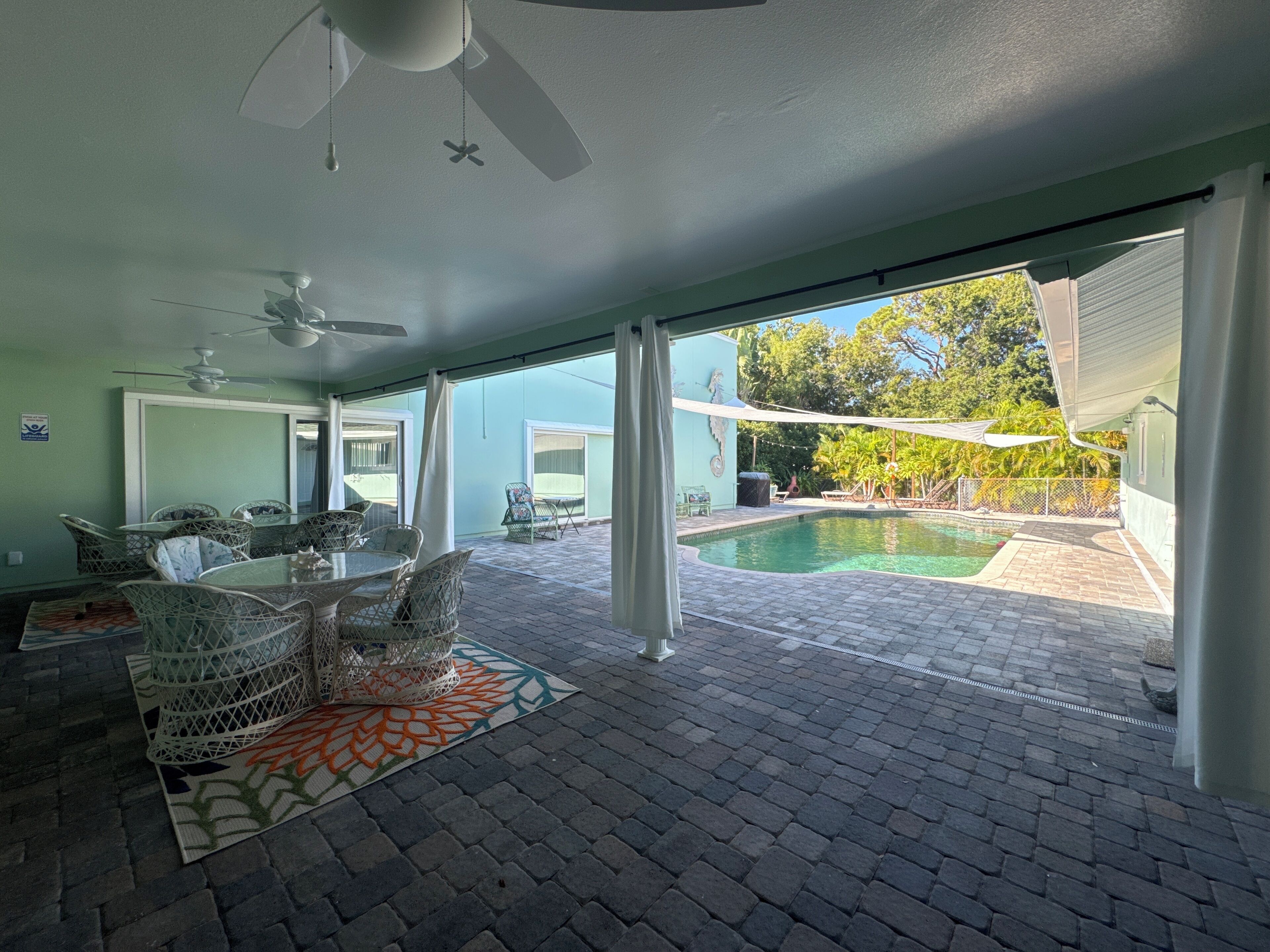 A spacious indoor area with a pool, a dining area with wicker furniture, and a ceiling fan.