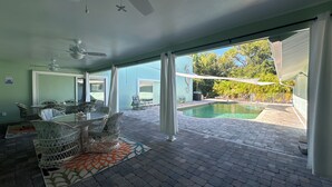 Un espacio interior amplio con piscina, zona de comedor con mobiliario de mimbre y ventilador de techo.