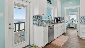 A kitchen with white cabinets, a tiled backsplash, and a view through a door to the outside.