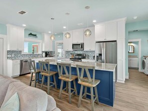 A modern kitchen with white cabinets, a blue island, and wooden bar stools.