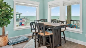 A dining area with a table and chairs, large windows, a ceiling fan, and a view of the ocean.