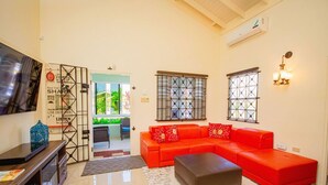 A living room with a red sofa, a grey ottoman, a TV, and a decorative wall with a message board. - 3BR Villa in Drax Hall Country Club (St. Ann's Bay)