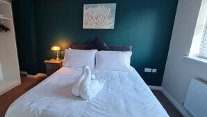 A neatly made bed with white linens and a white towel, a bedside lamp, and a wall-mounted artwork.