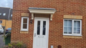 A two-story brick building with a white front door, two windows with shutters, and a small porch area.