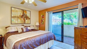 A bedroom with a large bed, a ceiling fan, a sliding glass door to a balcony, and artwork on the walls. - Par at Paradise in Palm Springs (Palm Springs)