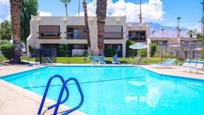 A swimming pool with blue chairs and a lifeguard stand, surrounded by palm trees and a building with balconies. - Par at Paradise in Palm Springs (Palm Springs)