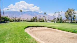 A golf course with a well-maintained green, sand bunkers, and a clear view of mountains in the background. - Par at Paradise in Palm Springs (Palm Springs)