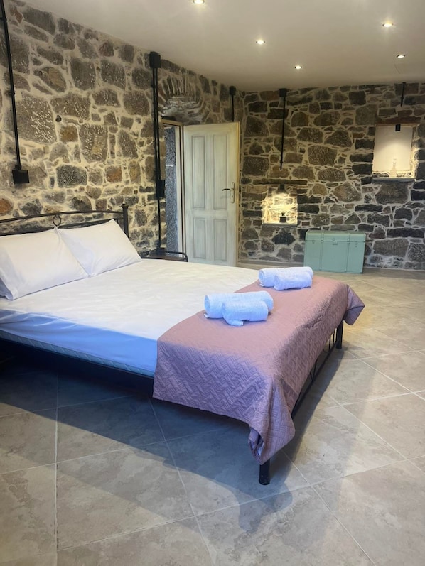 Een slaapkamer met een stenen muur, een bed met witte lakens en een stenen open haard.
