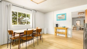 A modern dining area with a wooden table and chairs, a coffee machine, and a mirror on the wall.