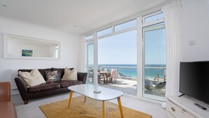 A living room with a large window, a brown leather sofa, a white coffee table, and a TV on a wooden cabinet. - Trewirgie - Central with sea views (St Ives)