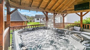 A hot tub under a wooden pergola with a view of houses in the background.