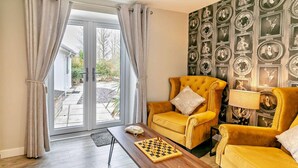 A room with a yellow armchair, a wooden coffee table with a chessboard, and a wall with framed pictures.