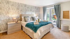 A bedroom with a large bed, a bedside table with a lamp, a nightstand, and a view of the outdoors through a sliding glass door.