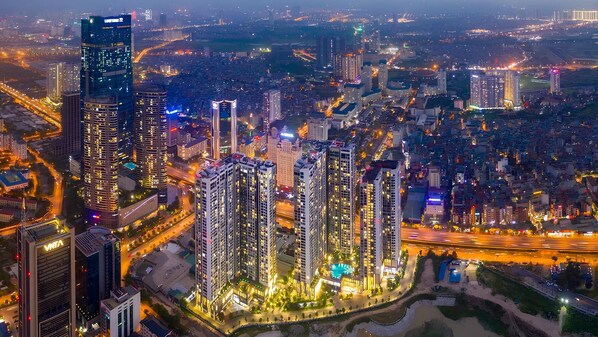 Un ensemble immobilier composé d’immeubles de grande hauteur, avec plusieurs tours, entouré d’un quartier urbain bien éclairé, où l’on aperçoit des rues et d’autres bâtiments.
