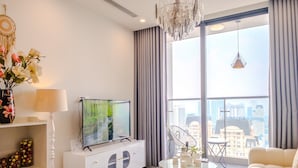 Ein modernes Wohnzimmer mit einem großen Fenster, einem Flachbildfernseher, einem weißen Sofa und einer Kristallleuchter.