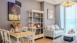 Ein modernes Wohnzimmer mit Essbereich, ausgestattet mit einem Holztisch, weißen Stühlen, einem gestreiften Sofa und einem Bücherregal.