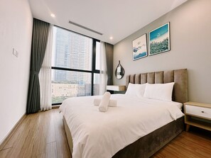 Une chambre d’hôtel moderne avec un grand lit, une table de chevet, un miroir et une vue sur les grands immeubles par la fenêtre.
