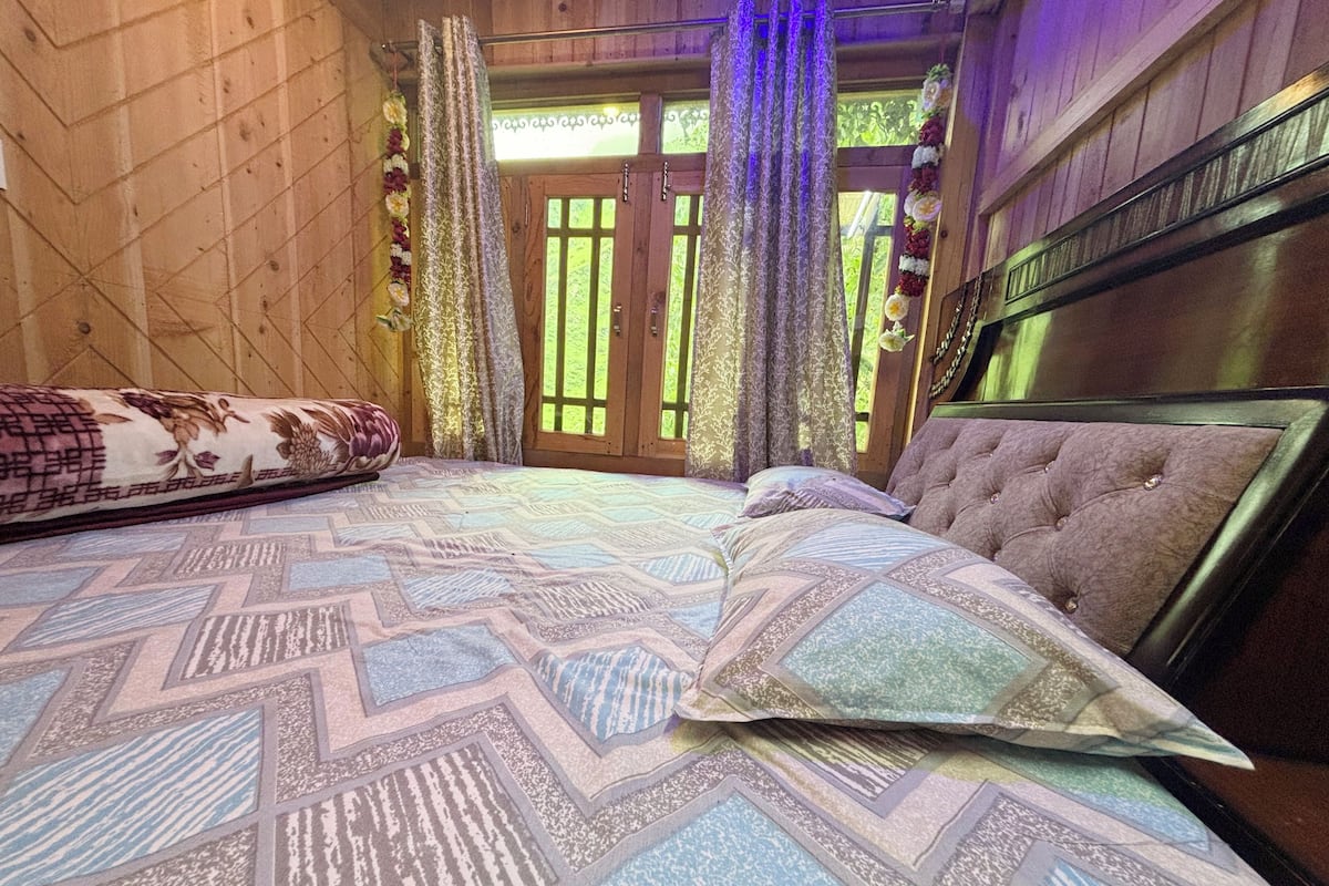 A bedroom with a bed, wooden walls, and a view through a window.