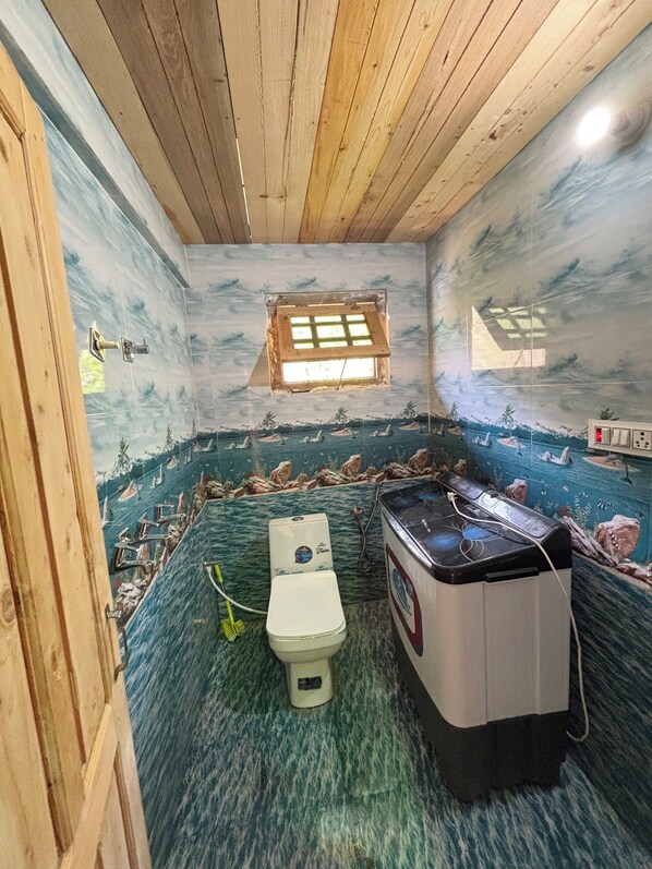 A room with a wooden ceiling, a small window, a toilet, and a washing machine.