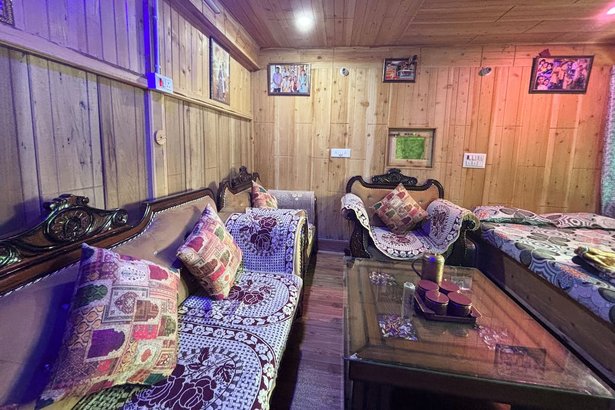 A cozy room with wooden walls, two wooden beds with patterned quilts, a wooden bench, and a glass coffee table with decorative items.